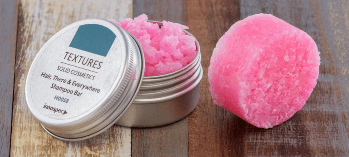 An aluminium tin containing pink chunks. A circular pink shampoo bar sits to the right of the tin.