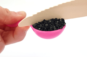 Photo showing a measuring spoon full of activated carbon being smoothed flat with the straight edge of the back of a knife.