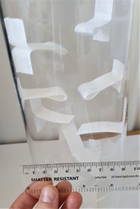 Close-up photo of a clear acrylic pipe with strips of adhesive hook tape stuck as flaps in various places down the pipe.